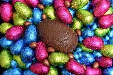 Yığınla renkli ve farklı boyutlarda renkli folyo paketlenmiş çikolatalı yumurtalar mavi, pembe, kırmızı, sarı ve limon yeşili ortasında büyük kahverengi sütlü çikolatalı yumurta.. 