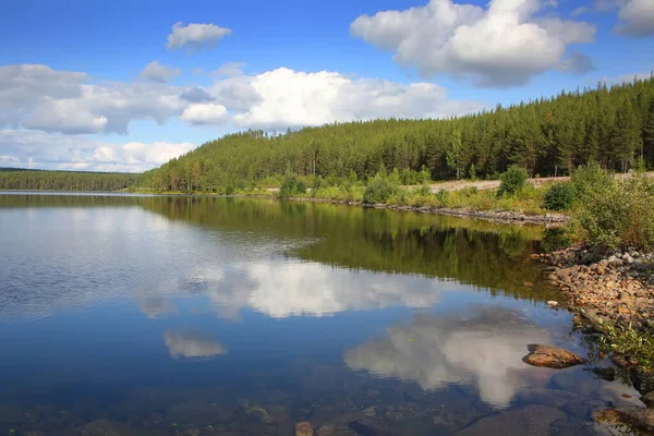 Beautiful landscape with a calm clear lake which has reflections of the trees and clouds. The lake lies within the Arctic circle near Polcirkeln, Northern Sweden, Scandinavia.