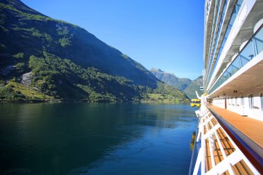 Yolcu gemisi güzel bir yaz gününde yumuşakça suya iniyor. Fiyorttaki dağların yansımaları. Norveç 'in Geiranger kasabası üzerinde tepeleri yükselen yemyeşil bir manzara.. 