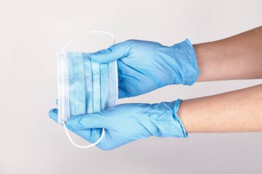 Gri arka planda solunum cerrahisi maskesi tutan tek kullanımlık mavi eldivenli eller. Pandemik korona virüsü, sigorta, hava hastalıkları, SARS, grippe. 