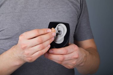 İşitme cihazı kullanan adam, yakın plan. Gri arka planda işitme cihazları, ameliyata alternatif. 