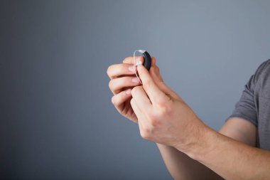 İşitme cihazı tutan adam, yakın plan. Gri arka planda işitme cihazları, ameliyata alternatif. İşitme cihazı hazır, ses bilimci. 