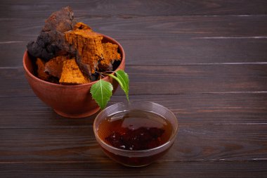 Ağaç dalı bir kase içinde doğal Chaga mantar parçaları ve koyu ahşap arka planda sıcak bitkisel çay, yakın çekim. Inonotus Obliquus. 