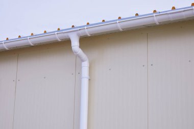 Beyaz plastik yağmur oluğu sistemi. Kanalizasyon borusu dış yüzeyde. Sandviç panelinin arka planı 