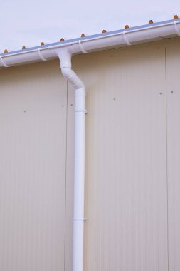 Beyaz plastik yağmur oluğu sistemi. Kanalizasyon borusu dış yüzeyde. Sandviç panelinin arka planı 