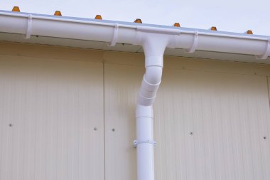 Beyaz plastik yağmur oluğu sistemi. Kanalizasyon borusu dış yüzeyde. Sandviç panelinin arka planı 