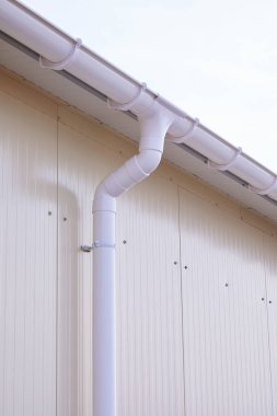 Beyaz plastik yağmur oluğu sistemi. Kanalizasyon borusu dış yüzeyde. Sandviç panelinin arka planı 