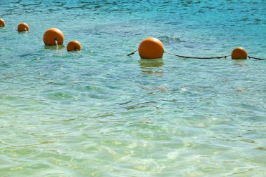 Buoys in the sea. View of the sea from a shore with a long line of orange colored marker buoys floating
