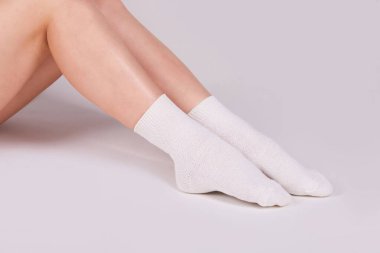Female legs in white cotton socks on white background. Ladies wearing sports socks