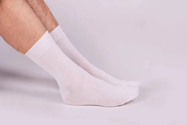 Man wearing new white cotton blank socks on a white background. Detailed closeup studio shot. Male legs wearing socks