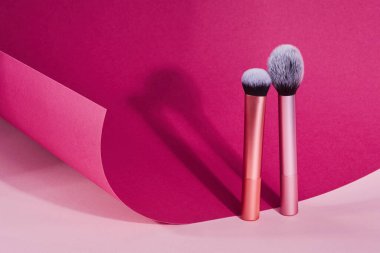 Pembe ve bordo kağıt arka planda makyaj fırçaları. Profesyonel Kozmetik Makyaj Fırçaları