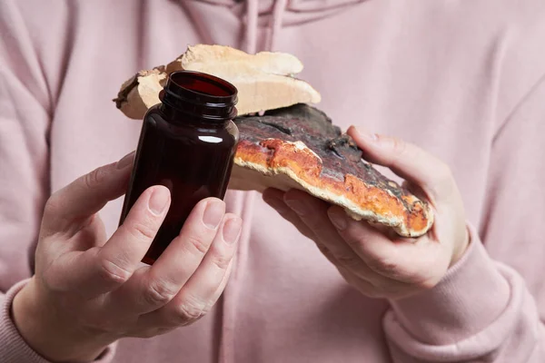 Dilimlenmiş Reishi mantarı (Ganoderma Lucidum olarak da bilinir) ve haplı koyu cam şişe tutan kadın elleri