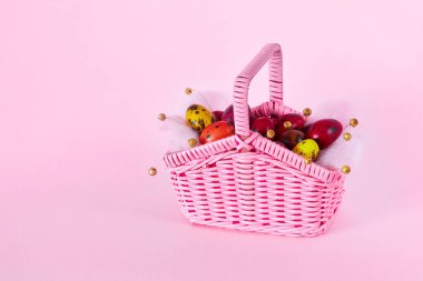 Colofrul bıldırcın yumurtaları pembe arka planda küçük pembe bir hasır sepette. Mutlu Paskalya kutlamaları. İlkbahar