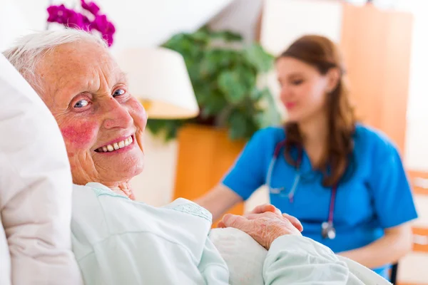 Felice donna anziana sdraiata a letto con un'infermiera premurosa — Foto Stock