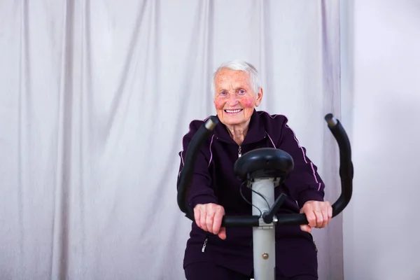 Seniorin auf stationärem Fahrrad — Stockfoto