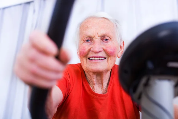Glad, eldre kvinne som spinner på en stasjonær sykkel – stockfoto