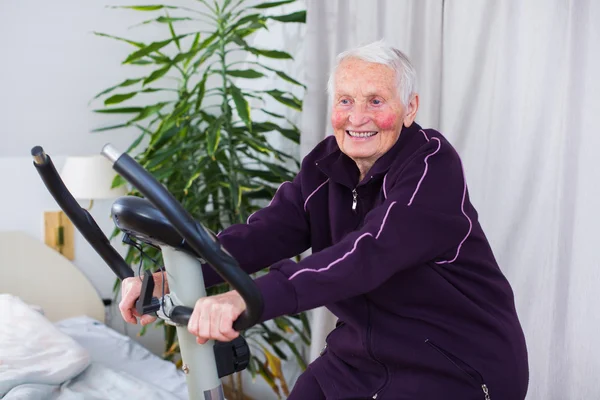 Seniorin auf stationärem Fahrrad — Stockfoto