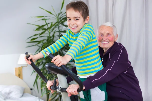 Mormor utbildning på stationär cykel med barnbarn — Stockfoto