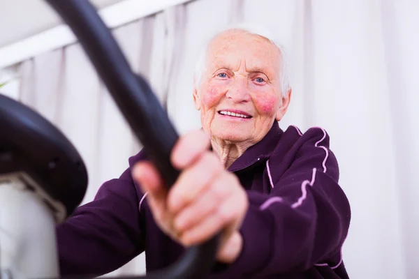 Seniorin auf stationärem Fahrrad — Stockfoto