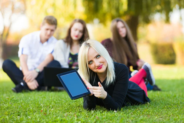 学生指着一款平板电脑与她的朋友们的草地上 — 图库照片