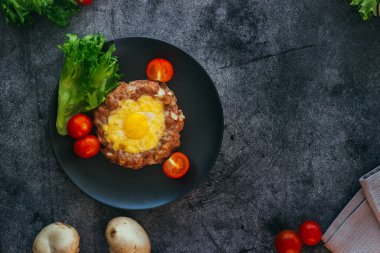 Tabakta yumurtalı biftek. Lezzetli sıcak yemek. Yemek kiraz domatesleri ve otlarla süslenmiş. Tabakta biftek. 