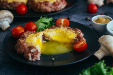Tabakta yumurtalı biftek. Lezzetli sıcak yemek. Yemek kiraz domatesleri ve otlarla süslenmiş. Tabakta biftek. 