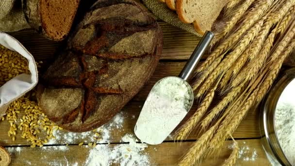 Pão, bainha de espigas de trigo e farinha em uma mesa de madeira, boneca, vista superior — Vídeo de Stock
