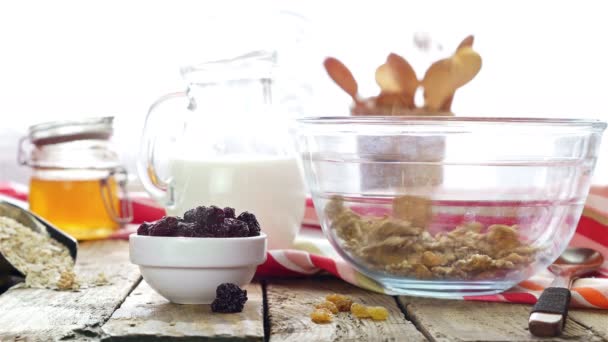 Granen en gedroogde vruchten zijn gegoten in een ontbijt kom, melk, honing en gedroogde vruchten op tafel — Stockvideo