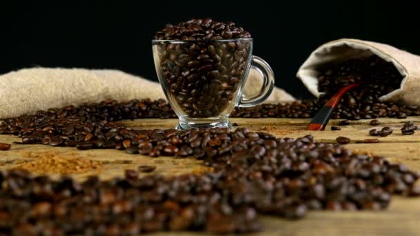 Weg mit Kaffeebohnen auf Holztisch, Tasse und Beutel mit Kaffeebohnen im Hintergrund, den Fokus ändern — Stockvideo