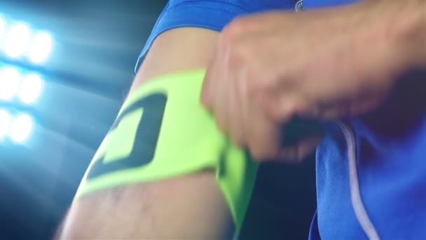 Football, soccer game. Professional footballer in blue outfit putting captain tape, black background — Stock Video