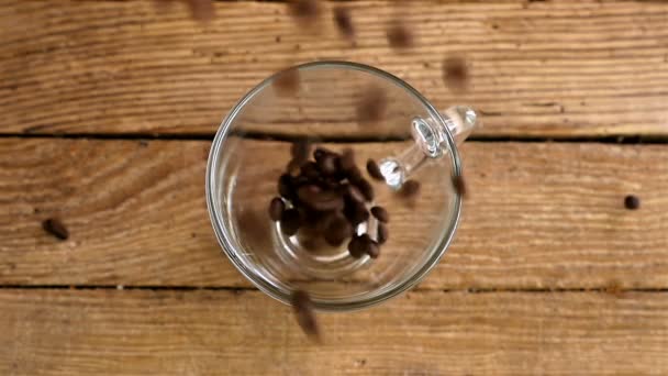 Slow motion gieten koffiebonen in een beker op een oude houten tafel, bovenaanzicht — Stockvideo