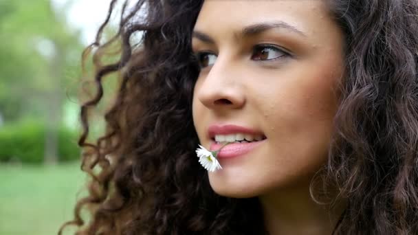 Retrato de una hermosa joven con hermoso pelo rizado con una margarita en la boca, cámara lenta — Vídeo de stock