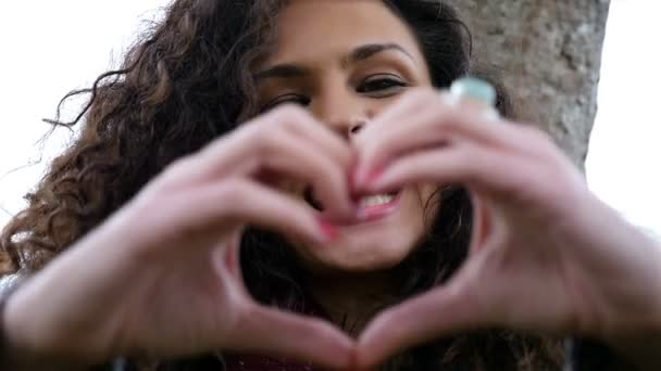 Retrato de mujer joven feliz con hermoso pelo rizado haciendo el gesto del corazón del amor con las manos en el parque, cámara lenta — Vídeos de Stock