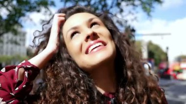 Şehirde gülümseyen güzel kıvırcık saçlı mutlu genç kadın portresi, yavaş hareket