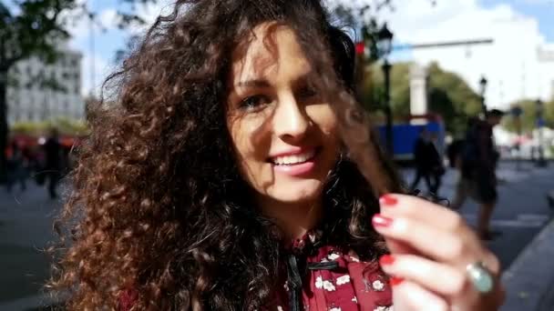 Şehirde gülümseyen güzel kıvırcık saçlı mutlu genç kadın portresi, yavaş hareket — Stok video
