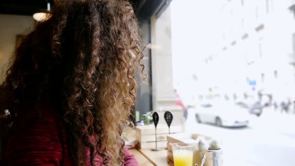 Портрет счастливой молодой женщины с красивыми вьющимися волосами, сидящей в кафе, замедленная съемка — стоковое видео