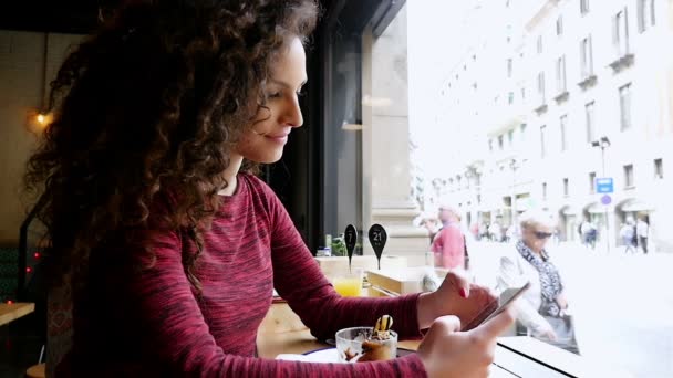 Portrait de jolie jeune femme utilisant un smartphone dans un café, au ralenti — Video