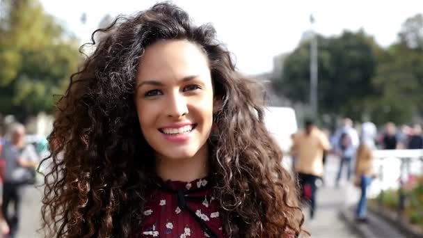 Retrato de uma jovem bonita com cabelo encaracolado sorrindo na cidade, câmera lenta — Vídeo de Stock