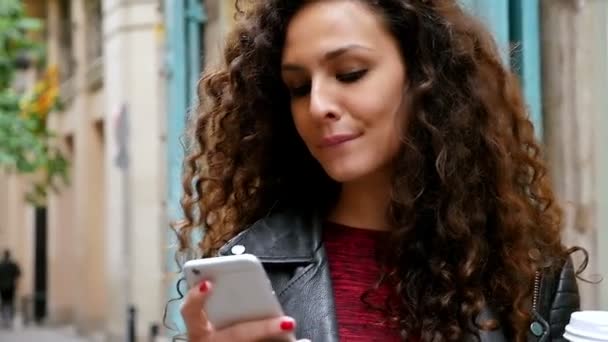 Портрет молодої жінки зі смартфоном, що йде вулицями міста, повільний рух — стокове відео