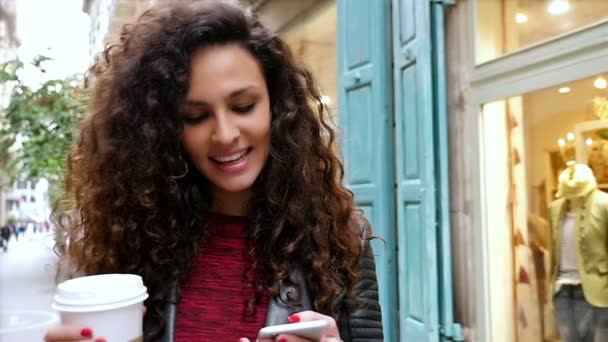 Portrait de jeune femme avec téléphone intelligent et café marchant dans les rues de la ville, ralenti — Video