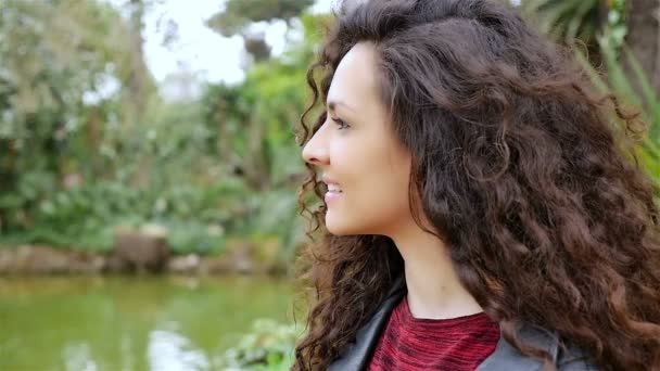 Retrato de uma jovem mulher feliz com belo cabelo encaracolado sorrindo em um parque, câmera lenta — Vídeo de Stock