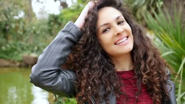 Portrait of a happy young woman with beautiful curly hair smiling in a park, slow motion — Stock Video