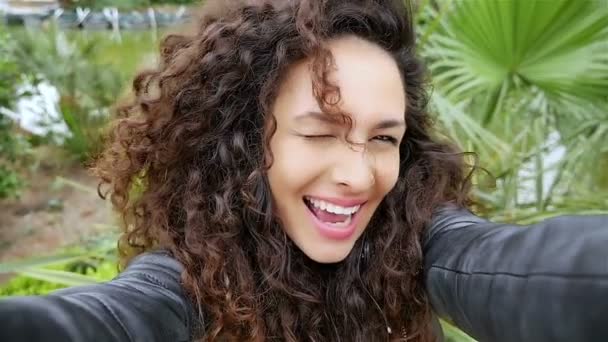 Portrait de jeune femme heureuse avec de beaux cheveux bouclés prenant selfie dans le parc, au ralenti — Video