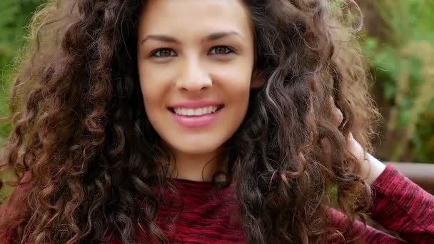 Портрет счастливой молодой женщины с красивыми вьющимися волосами, улыбающейся в парке, замедленная съемка — стоковое видео