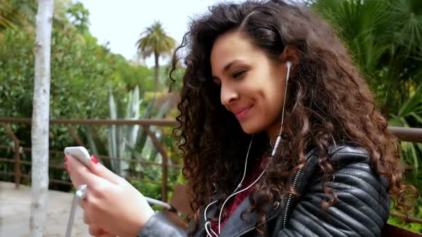 Jeune femme avec de beaux cheveux bouclés écoutant de la musique dans le parc, au ralenti — Video