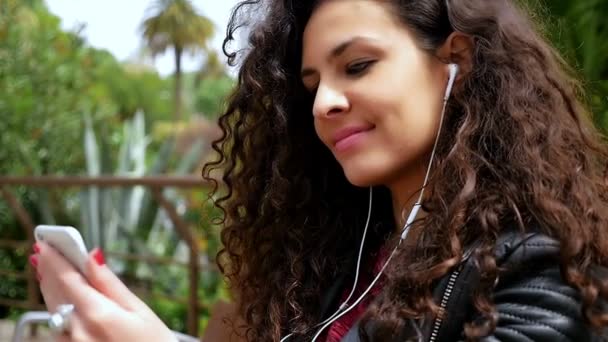 Fiatal nő gyönyörű göndör haj hallgat zenét a parkban, lassított felvétel — Stock videók