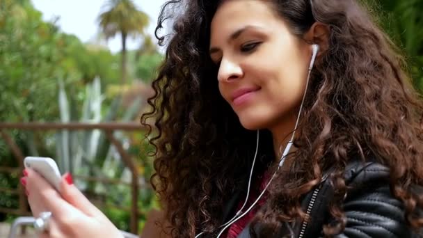 Young woman with beautiful curly hair listening to music in the park, slow motion — Stock Video