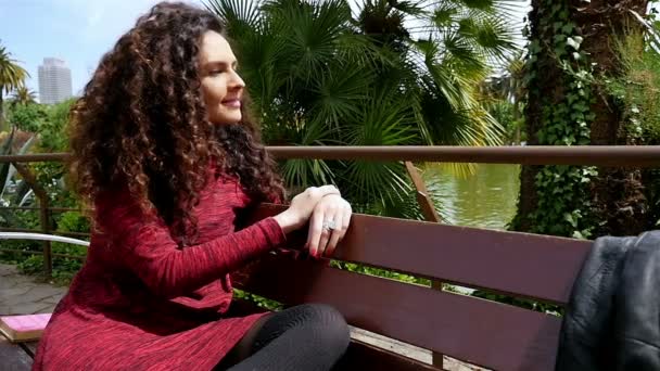 Portré egy boldog fiatal nő, gyönyörű göndör haja mosolyogva a parkban, lassított — Stock videók