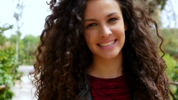 Retrato de uma jovem mulher feliz com belo cabelo encaracolado sorrindo em um parque, câmera lenta — Vídeo de Stock