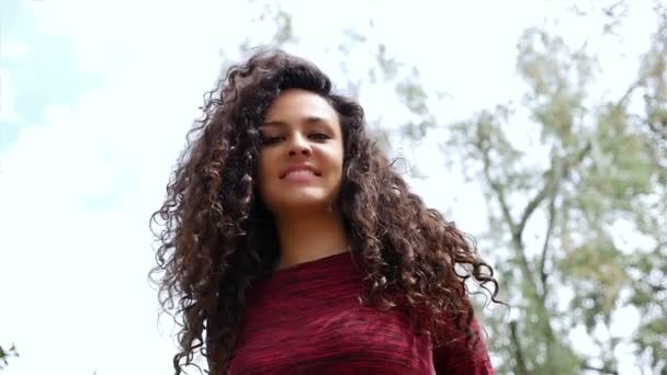 Портрет счастливой молодой женщины с красивыми вьющимися волосами, улыбающейся в парке, замедленная съемка — стоковое видео
